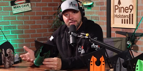 Pine 9 Holsters founder discussing fishing rod holster design during podcast recording while holding JettyHawk model with multiple holster colors displayed on desk microphone studio setup and brand signage in background showing product education and gear explanation content