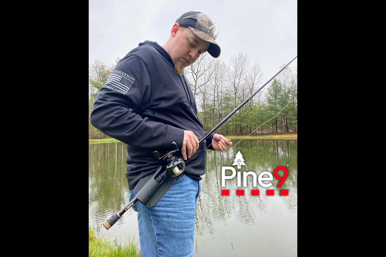 pine 9 JettyHawk fishing rod holster hands free hip rod hip holder man standing next to a pond putting his bait caster fishing rod in a holster